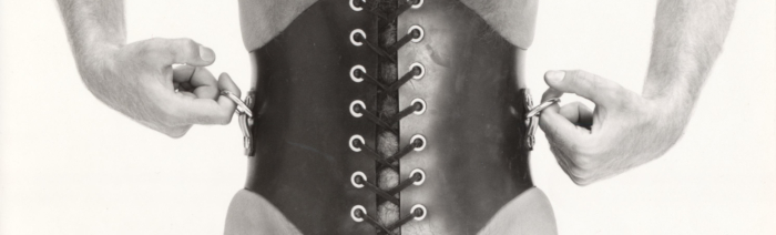 Photograph of a corseted male torso with hands holding side ring attachments.